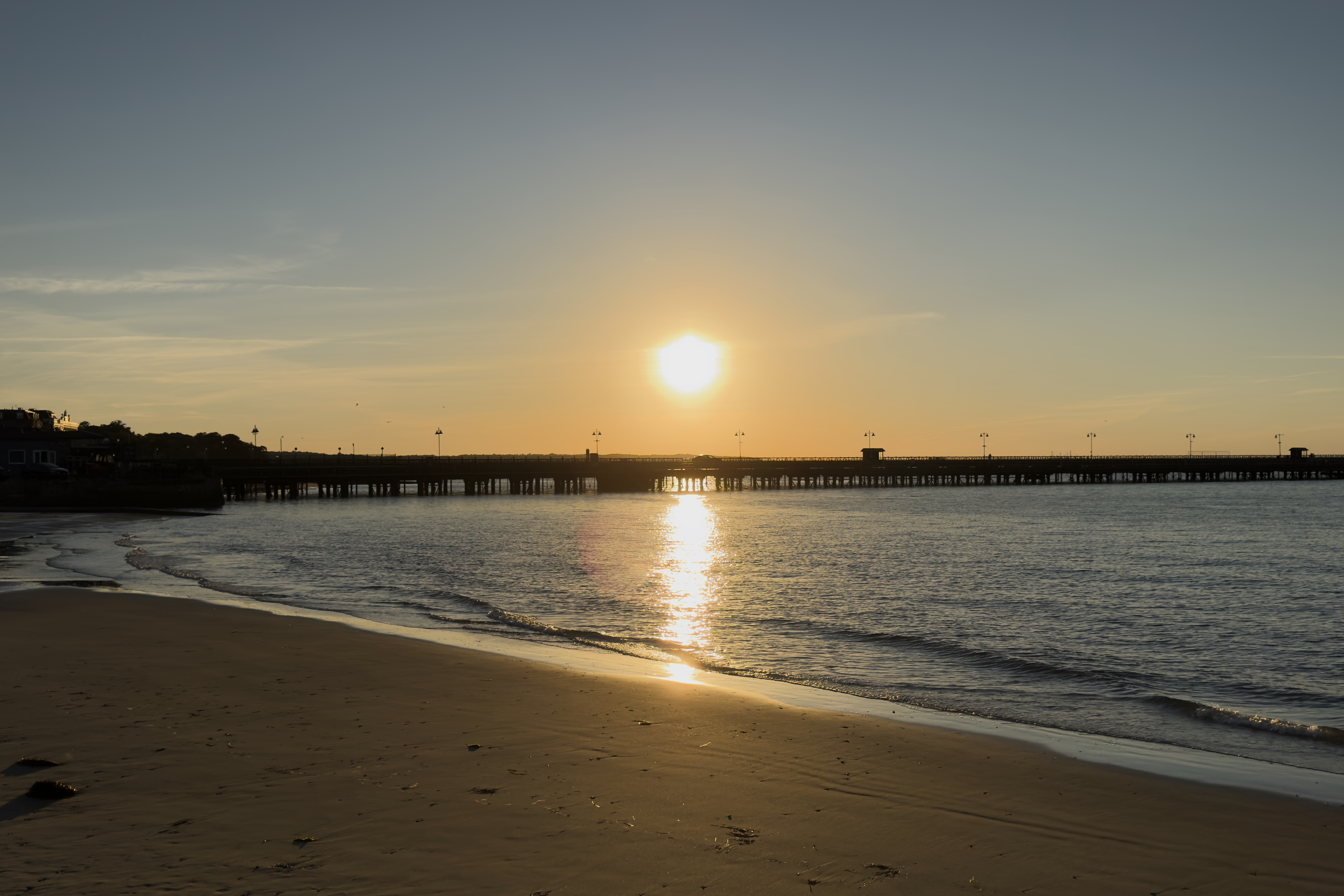 A pier stretching out into the sea at sunset with a few gulls overhead